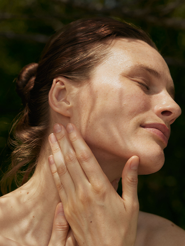 Frau pflegt Hals und Gesicht im Sonnenlicht