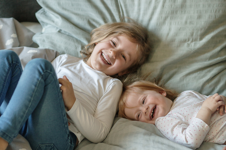 Zwei Kinder liegen lachend nebeneinander im Bett