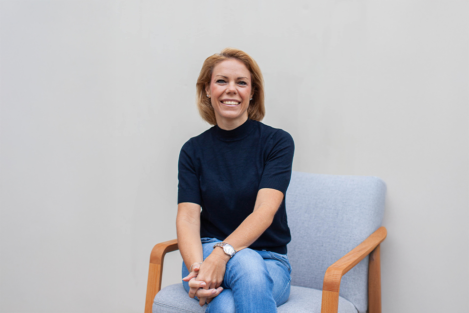 Frau sitzt auf Stuhl und lächelt freundlich in die Kamera