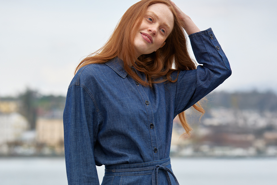Frau in blauem Mantel steht am Wasserufer