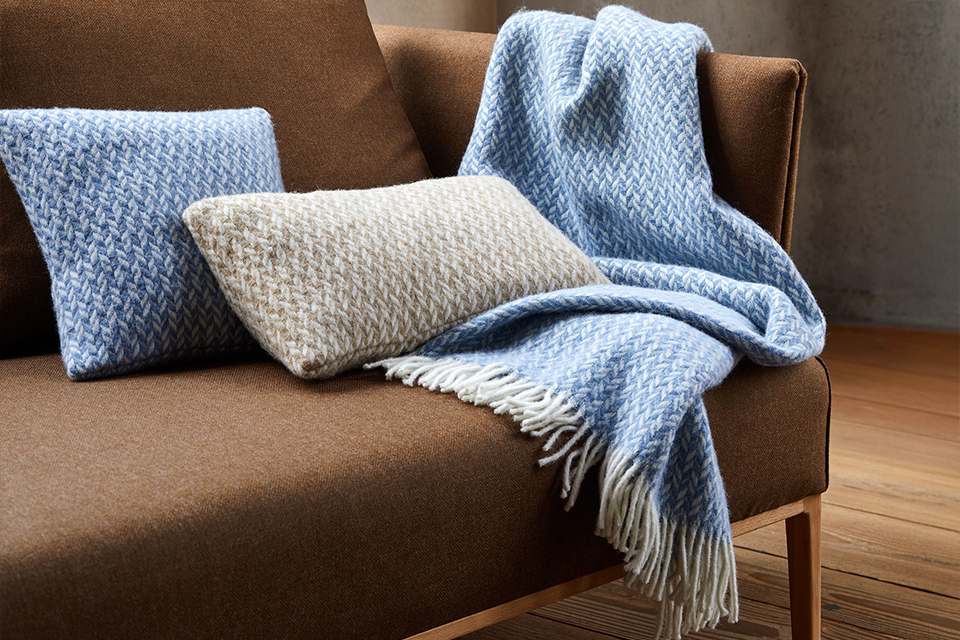 Zierkissen und Wohndecke auf einem braunen Sofa liegend