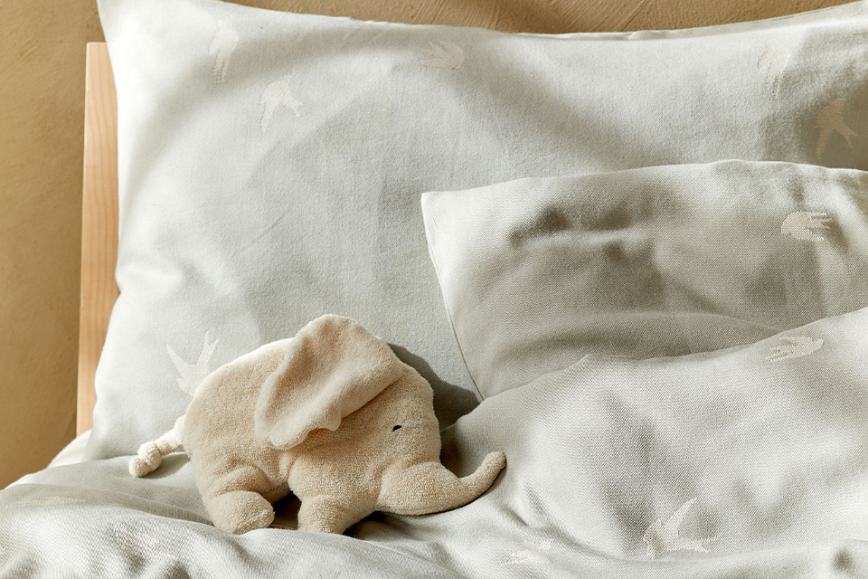 Weiße Bettwäsche mit einem kleinen Kuscheltierelefanten auf einem Bett