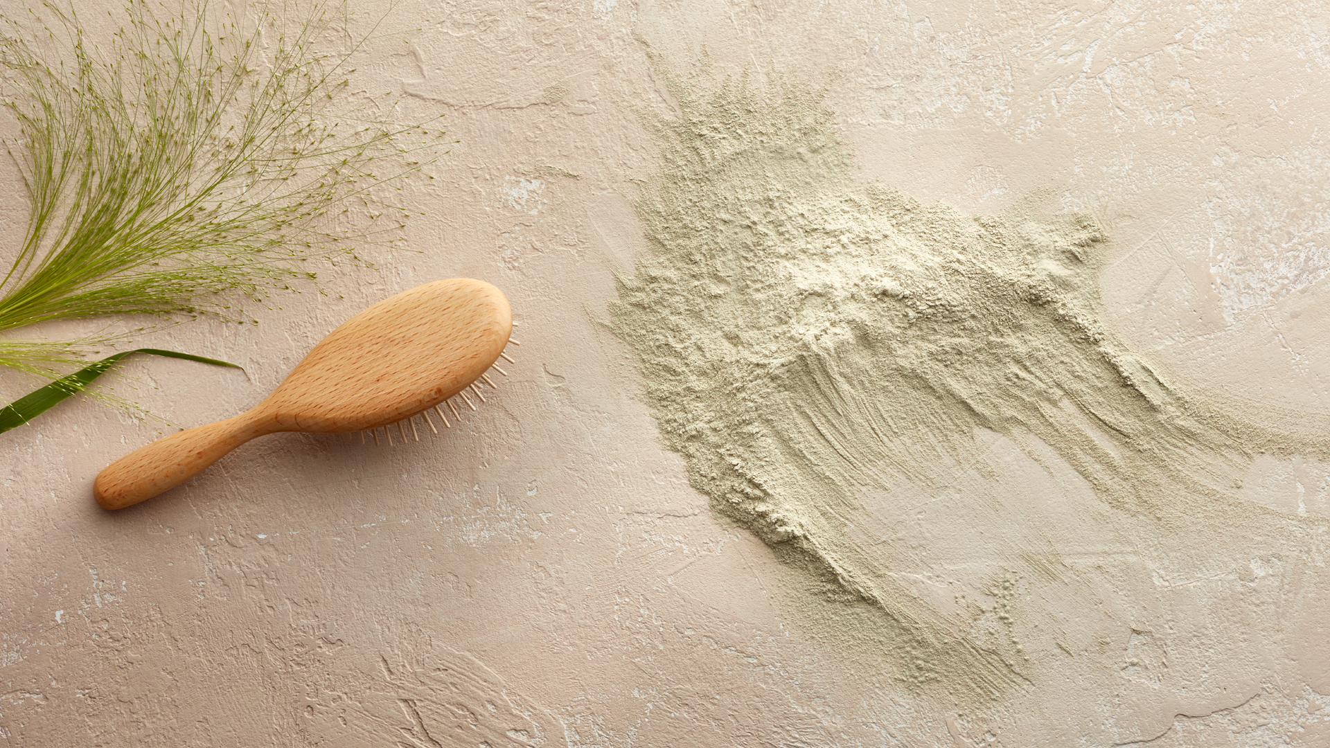 grünes Pulver und eine Haarbürste aus Holz auf hellem Untergrund