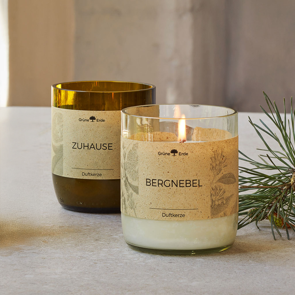 Zwei Duftkerzen auf hellem Untergrund mit dekorativem Zweig