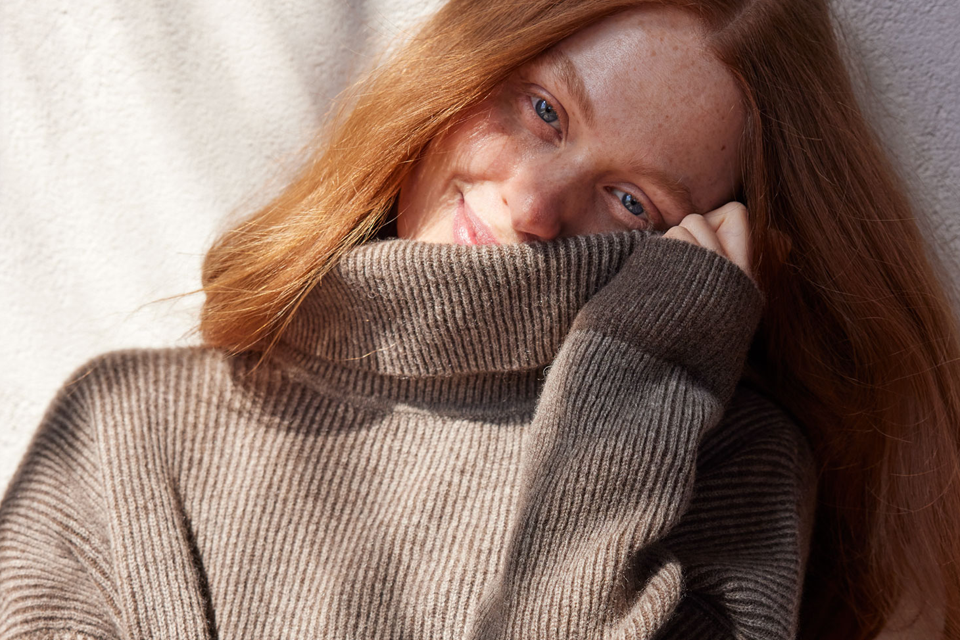 Frau in braunem Pullover neigt ihren Kopf zur Seite