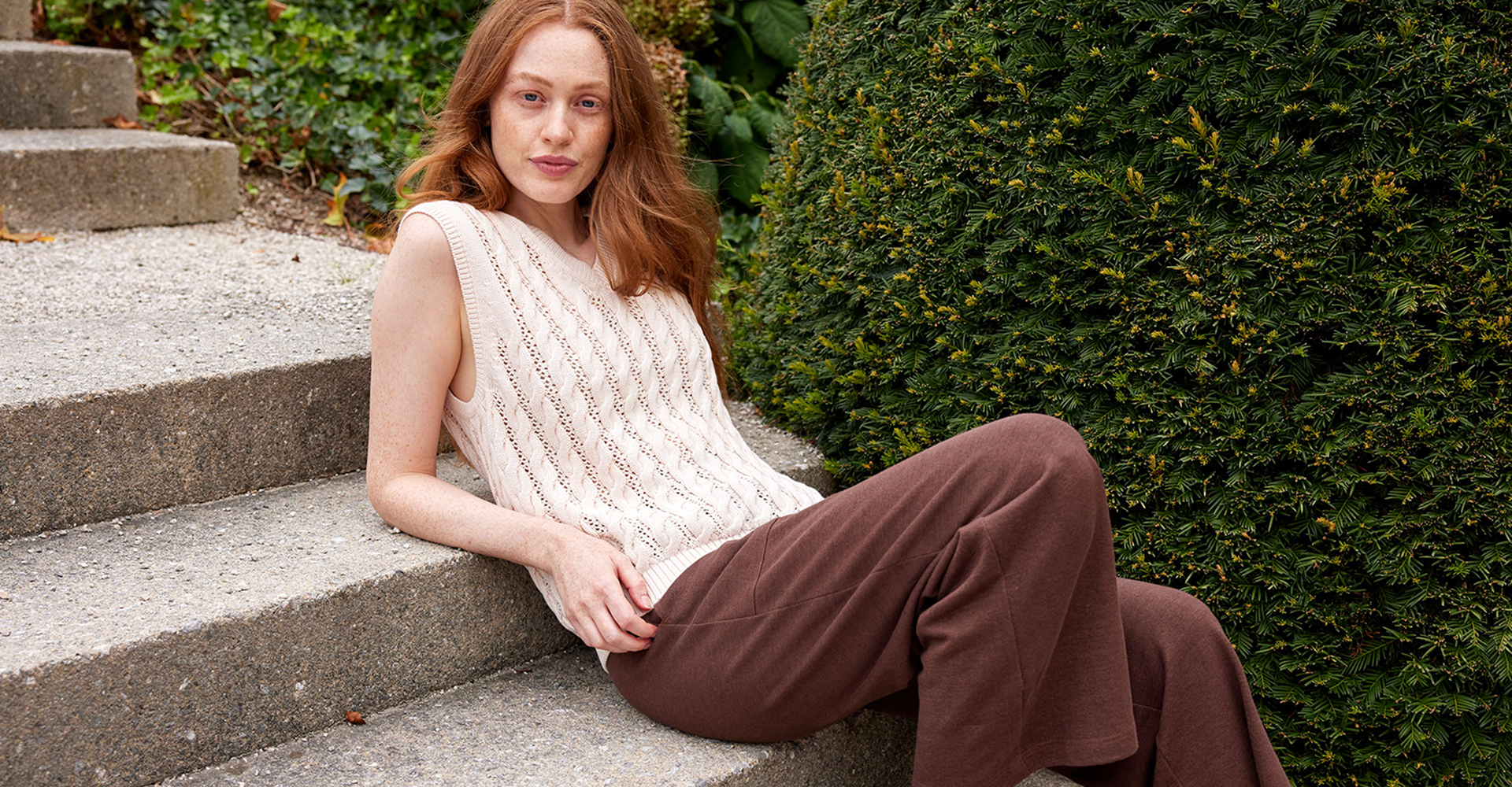 Frau trägt beigen Strickpullunder und braune Hose und sitzt auf Treppen