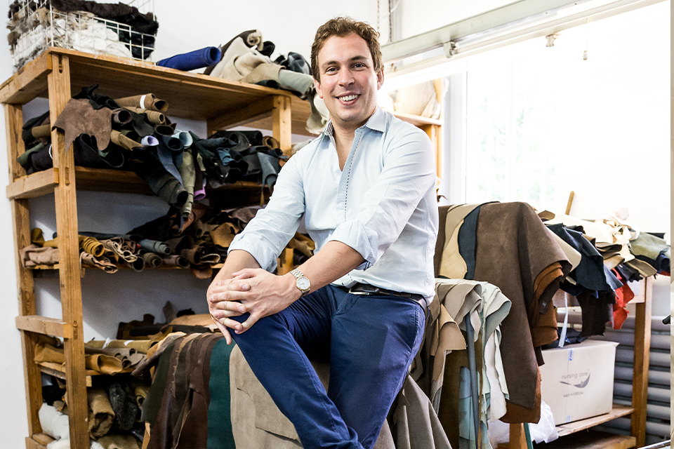 Mann sitzt lächelnd zwischen Stoffrollen und Leder in Werkstatt