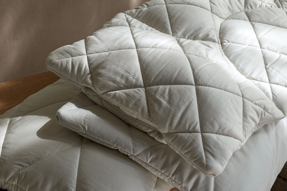 Drei Kopfkissen liegen auf einem Stapel auf einer Holzbank