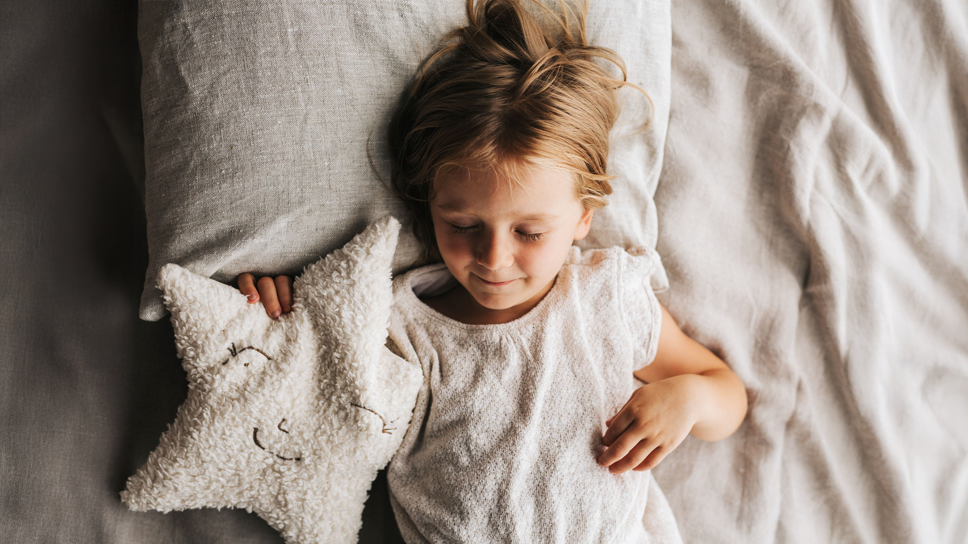 Kind liegt im Bett mit Kuschelkissen