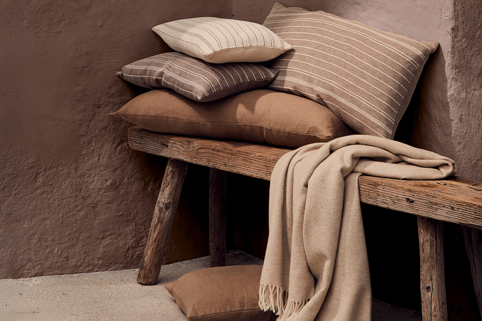 verschiedenfarbige Zierkissen und eine Wohndekce auf einer dekorativen Holzbank gestapelt