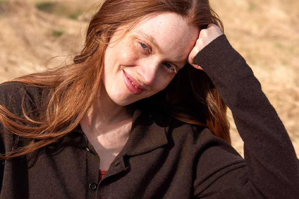 Frau im braunen Sweatshirt sitzt mit dKopf auf den Arm gestützt