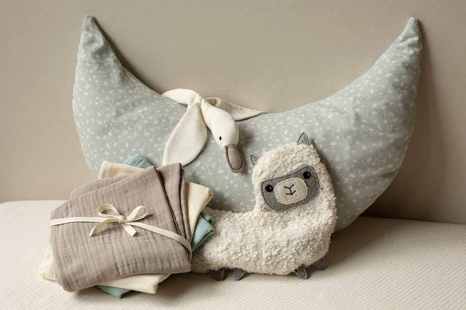 Halbmondkissen mit Kuscheltieren und Stoffwindetset aneinander arrangiert