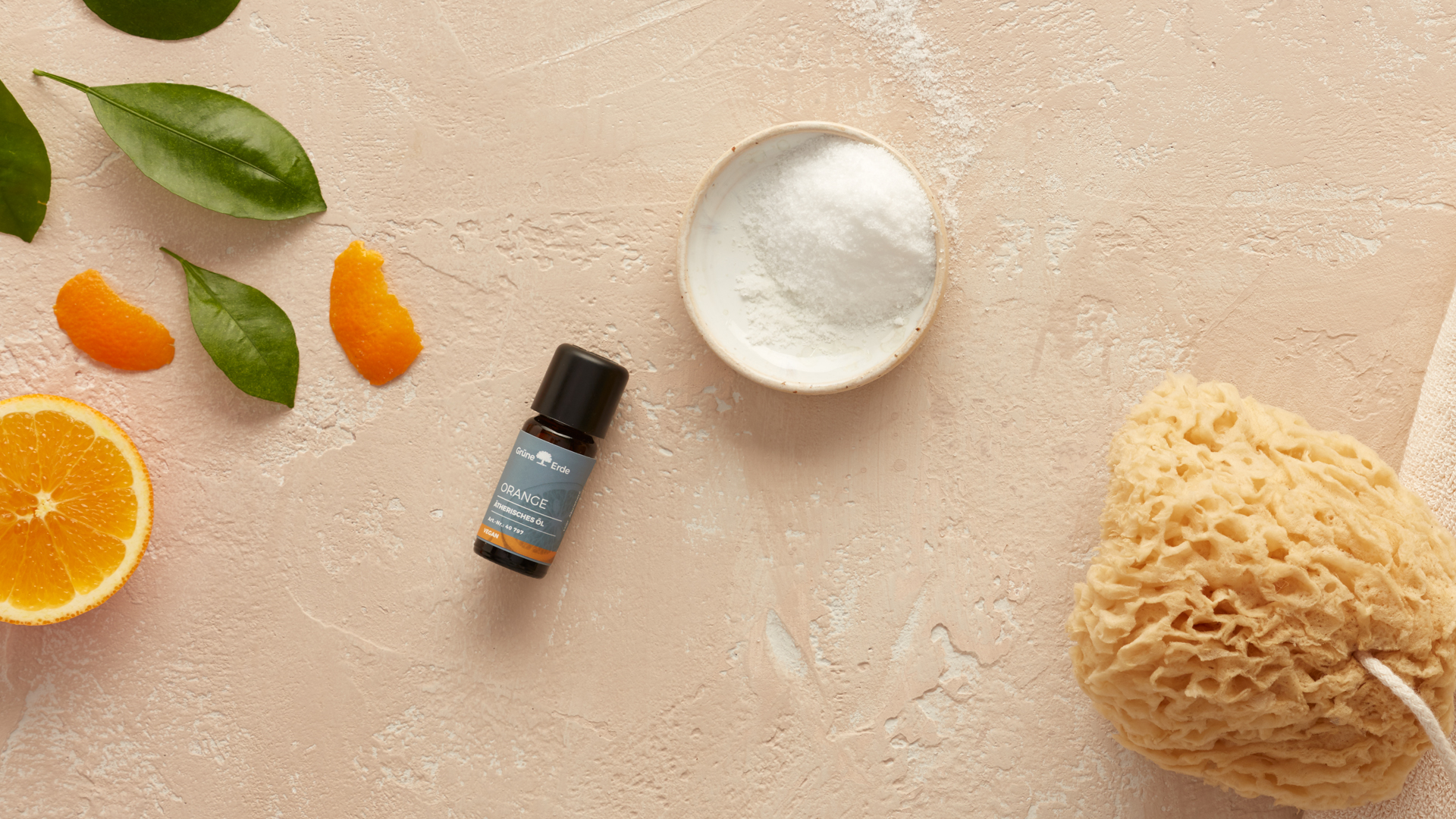 ätherisches Öl und Zucker neben einer Orange und einem Schwamm