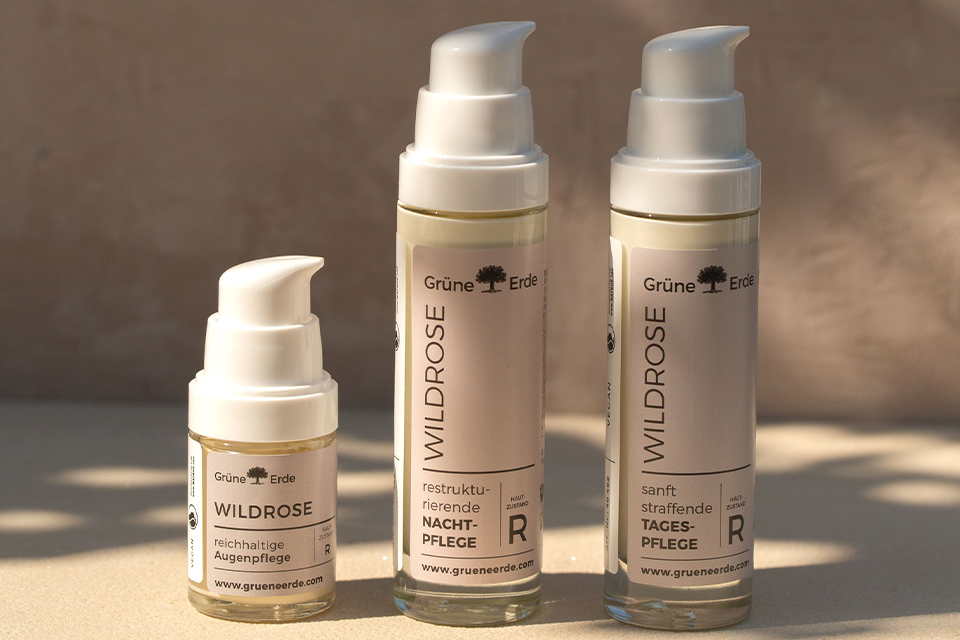 Drei Wildrose Hautpflegeflaschen mit Pumpspendern auf heller Oberfläche.