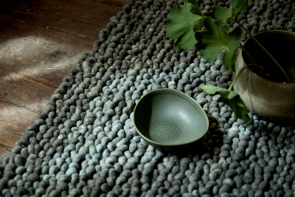 Dunkelgrüner Teppich mit einer Keramikschale und einer Vase auf dem Boden liegend