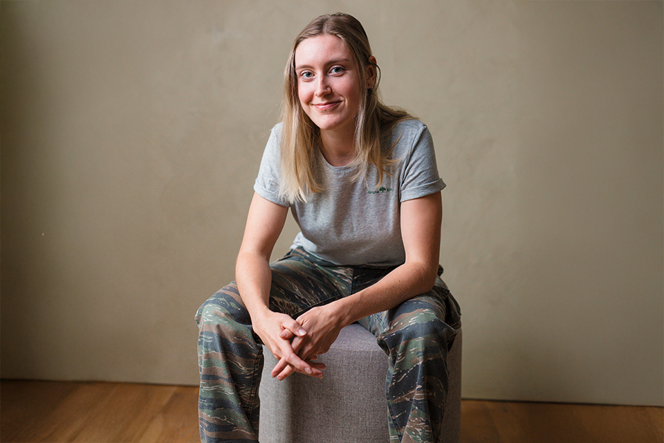 Junge Frau sitzt entspannt und lächelt in neutralem Raum