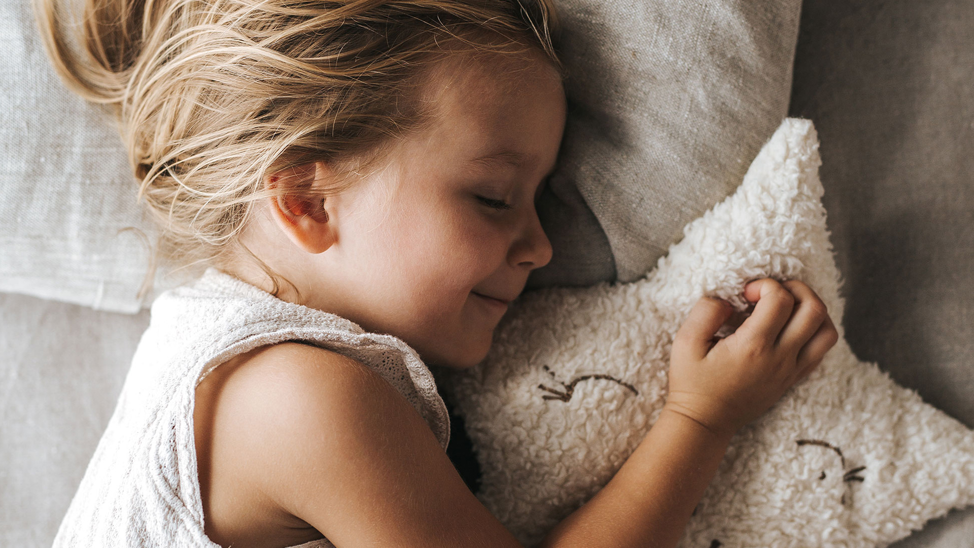 Kind schläft imBett mit einem Kuscheltier in der Hand