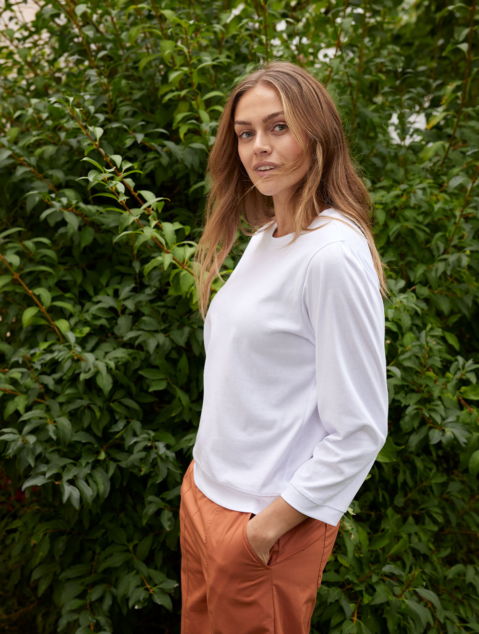 Frau trägt weißes Langarmshirt und orange Hose in natürlicher Umgebung