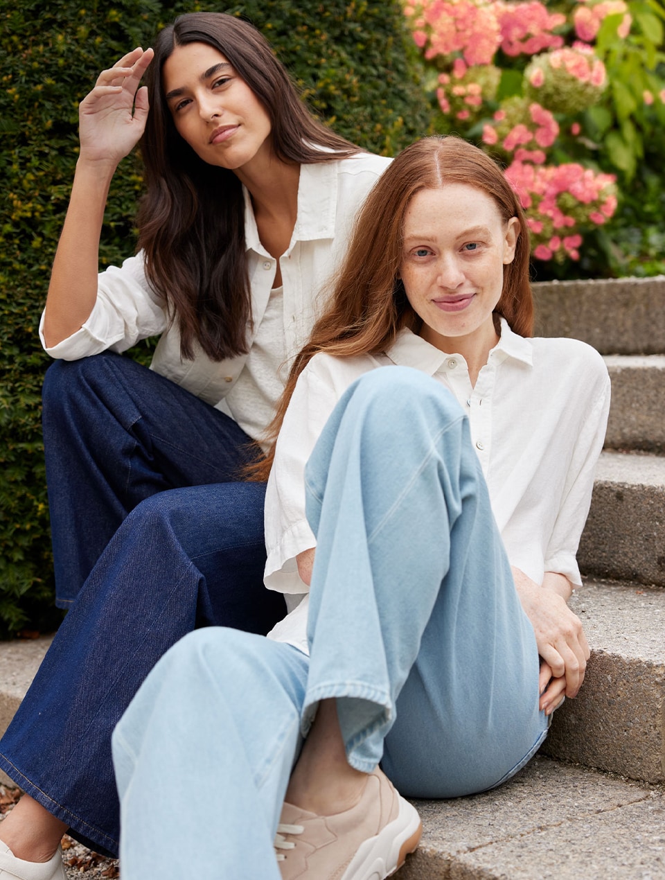 Zwei Frauen tragen weiße Blusen und Jeans und sitzen auf einer Treppe