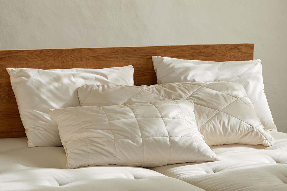 vier hochwertige Kopfkissen liegen in einem Massivholzbett auf einer Naturmatratze