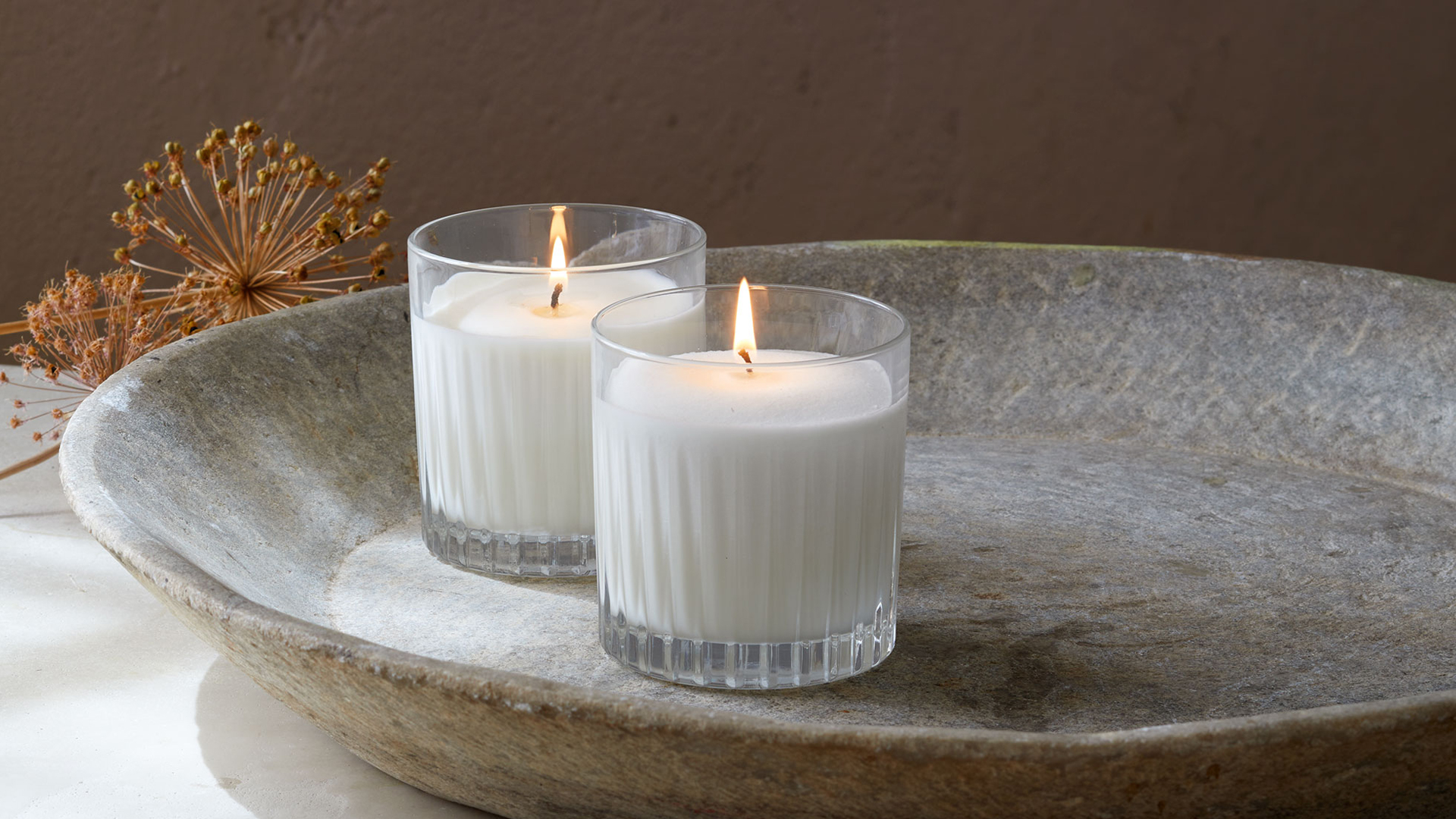 Zwei Duftkerzen in einer Kermaiksschale und dekorativen Blumen auf einem Tisch stehend