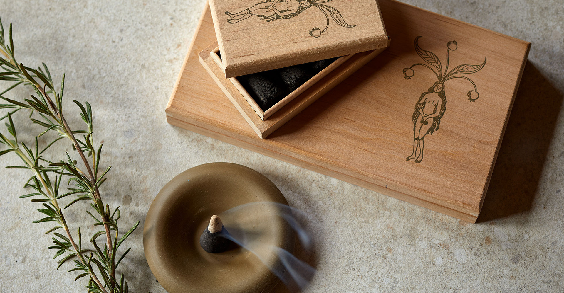 Räucherkegel mit Rauch auf Unterteller neben Holzbox und dekorativem Zweig in ruhiger Umgebung