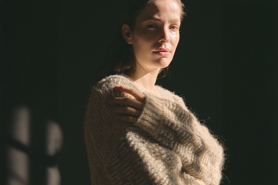 Frau im weichen Pullover steht im stimmungsvollen Licht