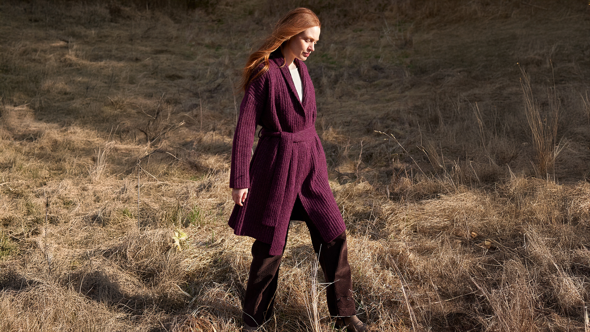 Frau in weiter Strickmode spaziert durch trockene Landschaft