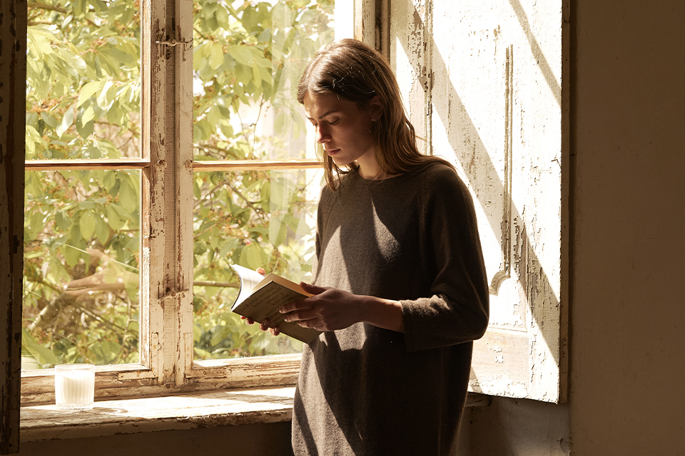 Frau liest achtsam am Fenster im warmen Sonnenlicht