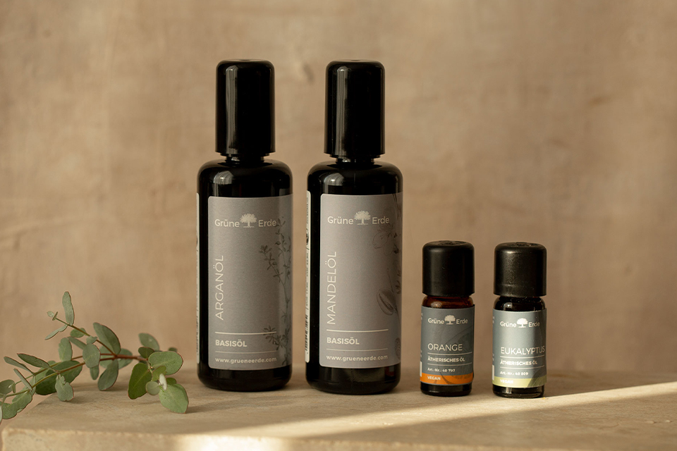 Zwei Basisöle und zwei Aromaöle neben einem dekorativen Zweig