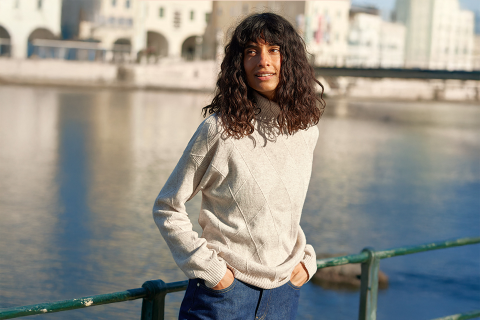 Frau in heller Kleidung steht am Wasser in Stadtnähe