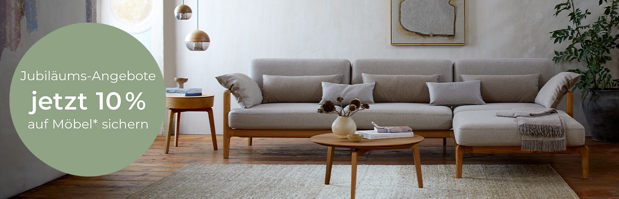 Man sieht ein Wohnzimmer, ein graues Sofa steht auf einem hellgrauen Teppich, davor ein Couchtisch aus Buchenholz
