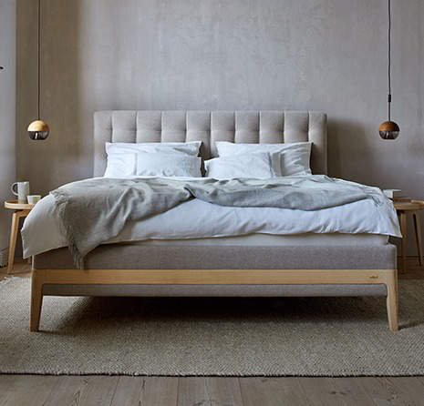 Bett Philomena in grau steht auf einem hellgrauen Teppich im Schlafzimmer