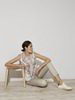 Model mit leichter Bluse mit geometrischem Druck und heller Hose am Boden sitzend