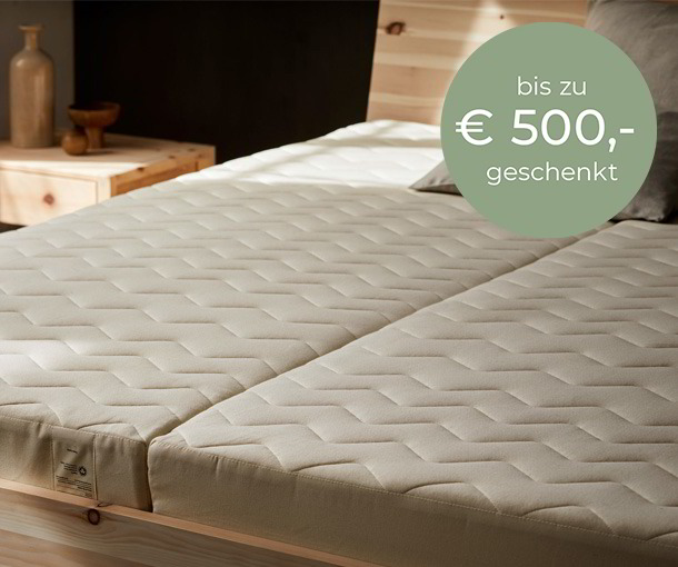 In einem Holzbett liegen zwei Gruene Erde Matrazten, bis zu 500 Euro geschenkt