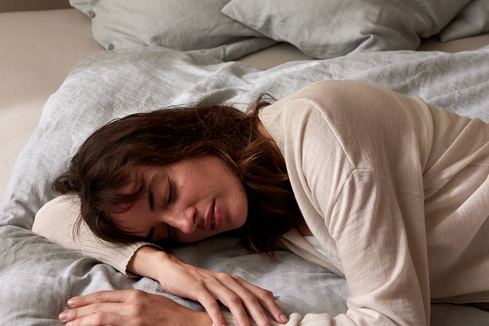 Eine Frau in Bauchlage mit hellem Shirt auf einer grauen Bettwäsche