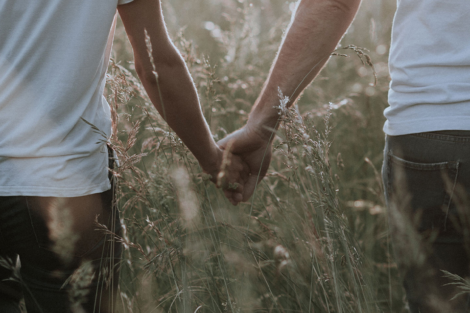 Zwei Menschen halten Hände im hohen Gras im Sommer