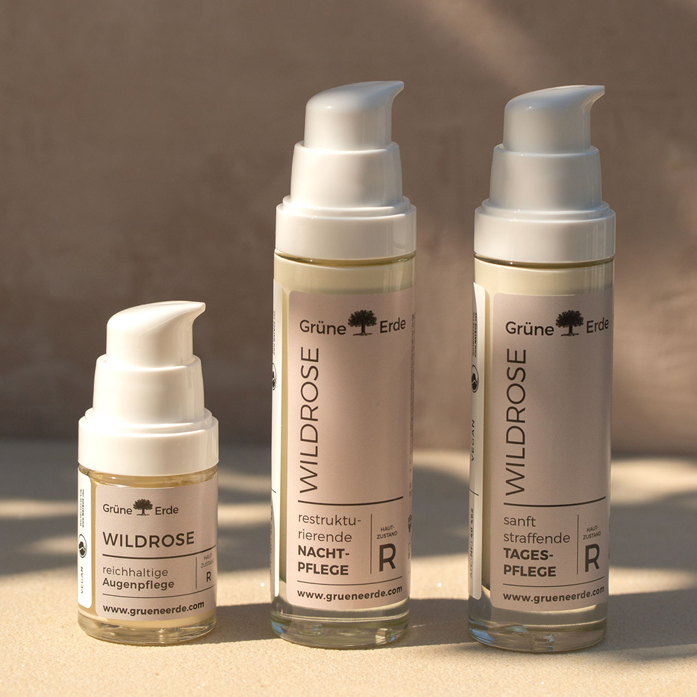 Drei Wildrose Hautpflegeflaschen mit Pumpspendern auf heller Oberfläche.