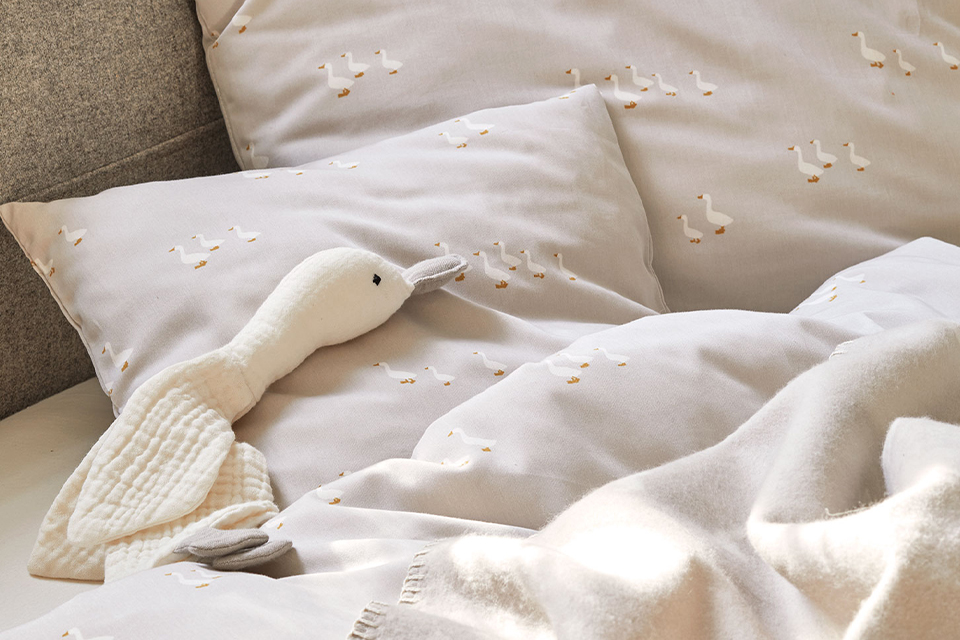Graue Bettwäsche mit Gänsemuster und Kuschelgans auf einem Bett