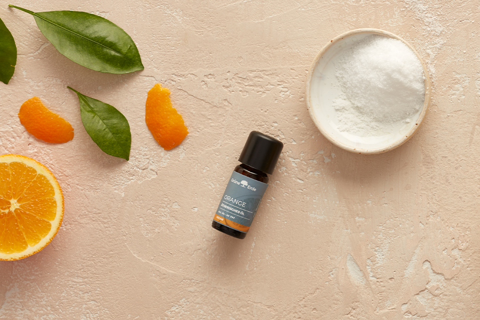 ätherisches Öl und Zucker neben einer Orange und dekorativen Blättern