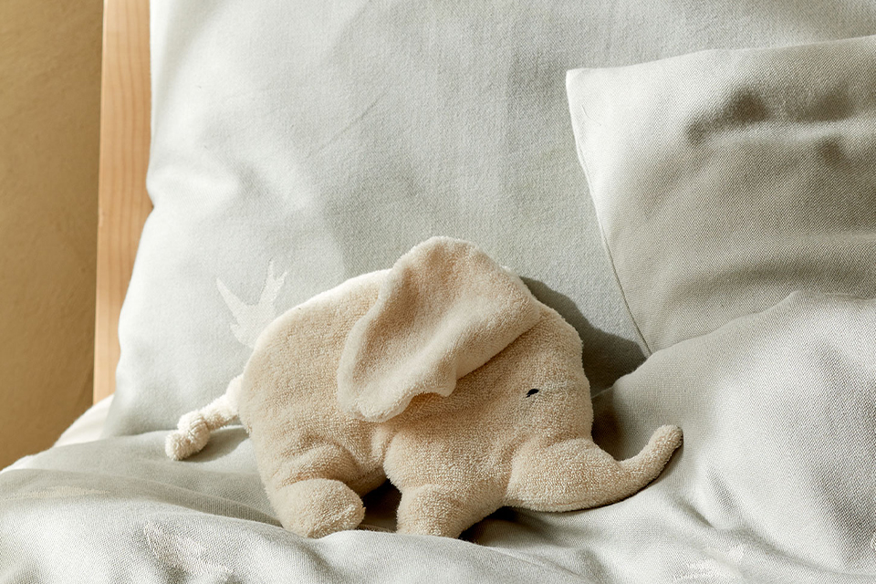 Weiße Bettwäsche mit einem kleinen Kuscheltierelefanten auf einem Bett