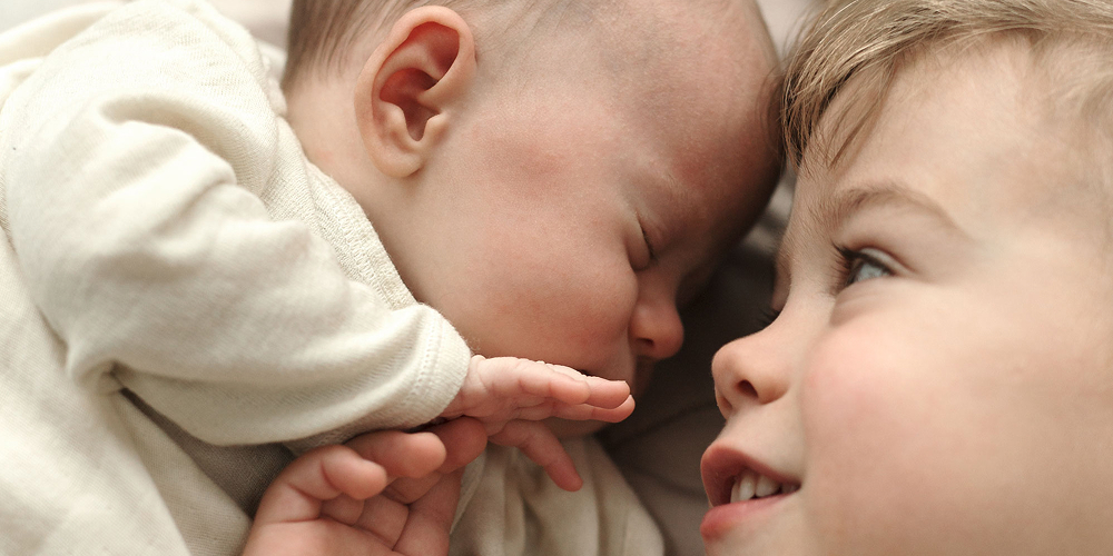Baby und Kind liegen auf einer Decke und lachen sich an