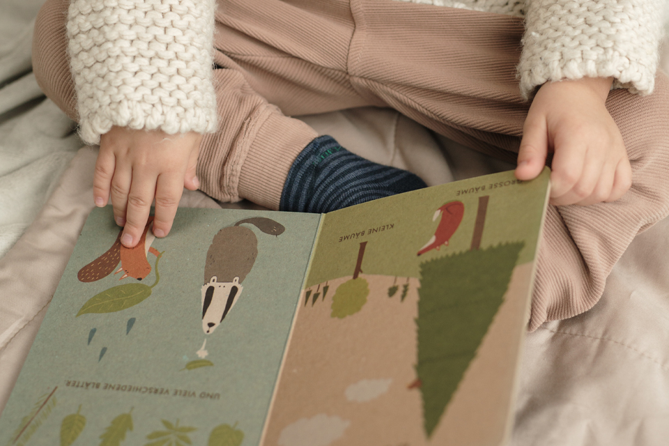 Kind blättert im Bilderbuch auf dem Bett sitzend