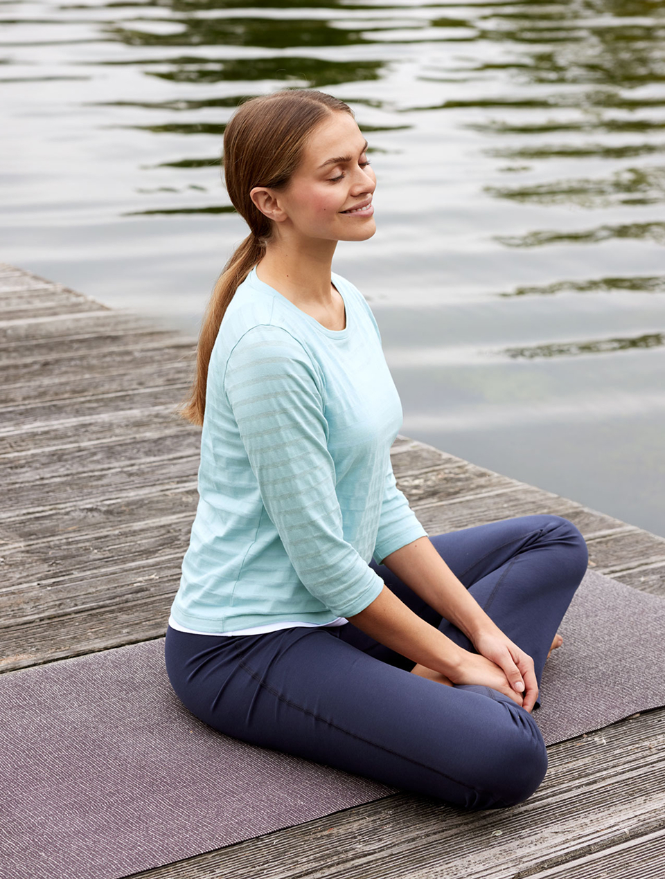 Frau trägt hellblaues Sweatshirt und Yogahose und sitzt am Wasser