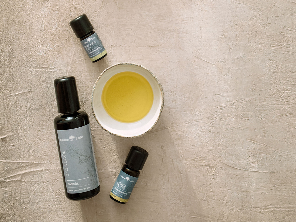 Ein Basisöl und zwei ätherische Öle liegen auf einer neutralen Oberfläche mit einem Schälchen mit Öl