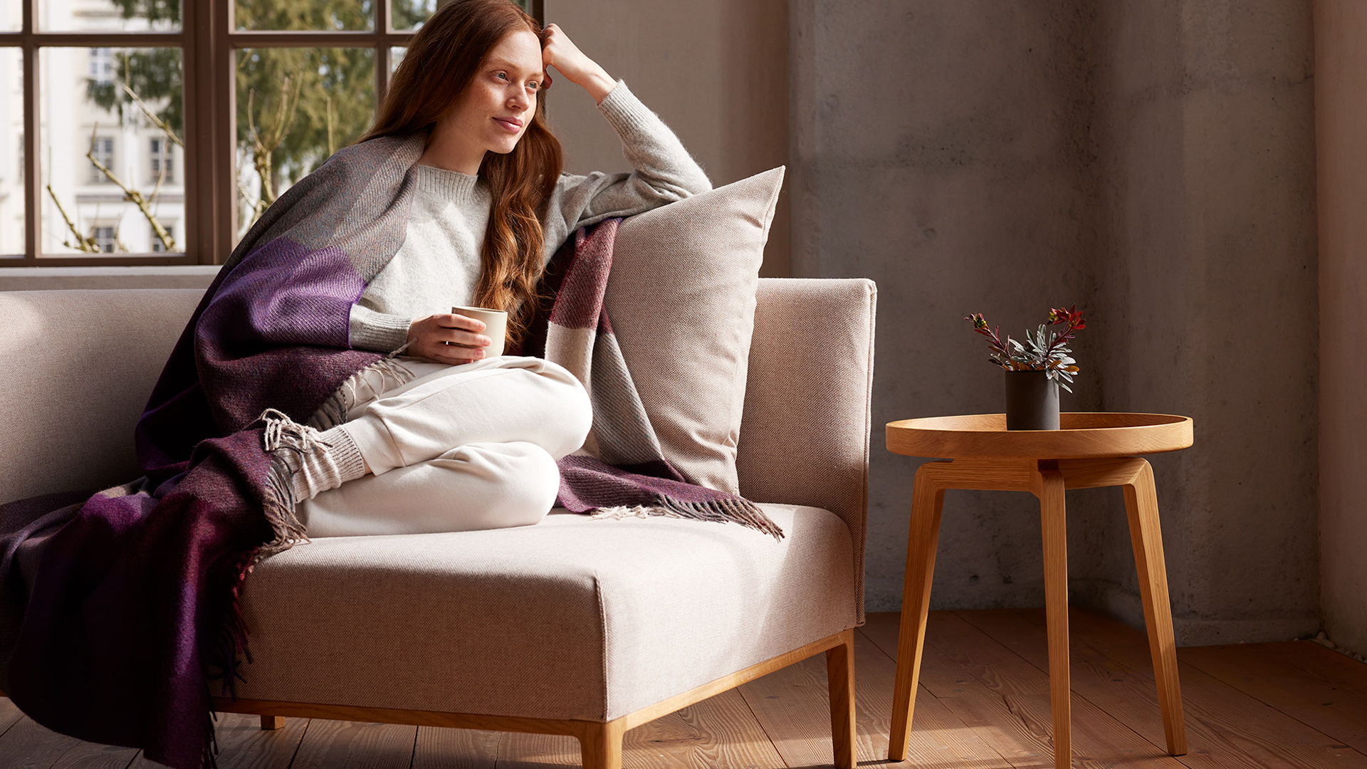 Frau in Wohndecke gehüllt auf einem Sofa sitzend