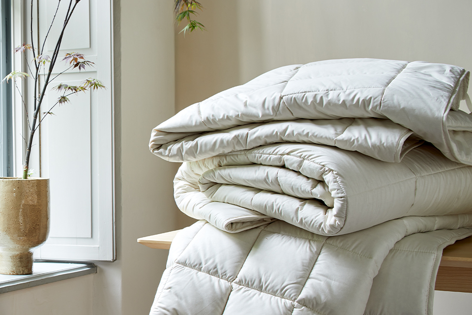 Ökologische Bettdecken auf einem Holztisch vor einem Fenster