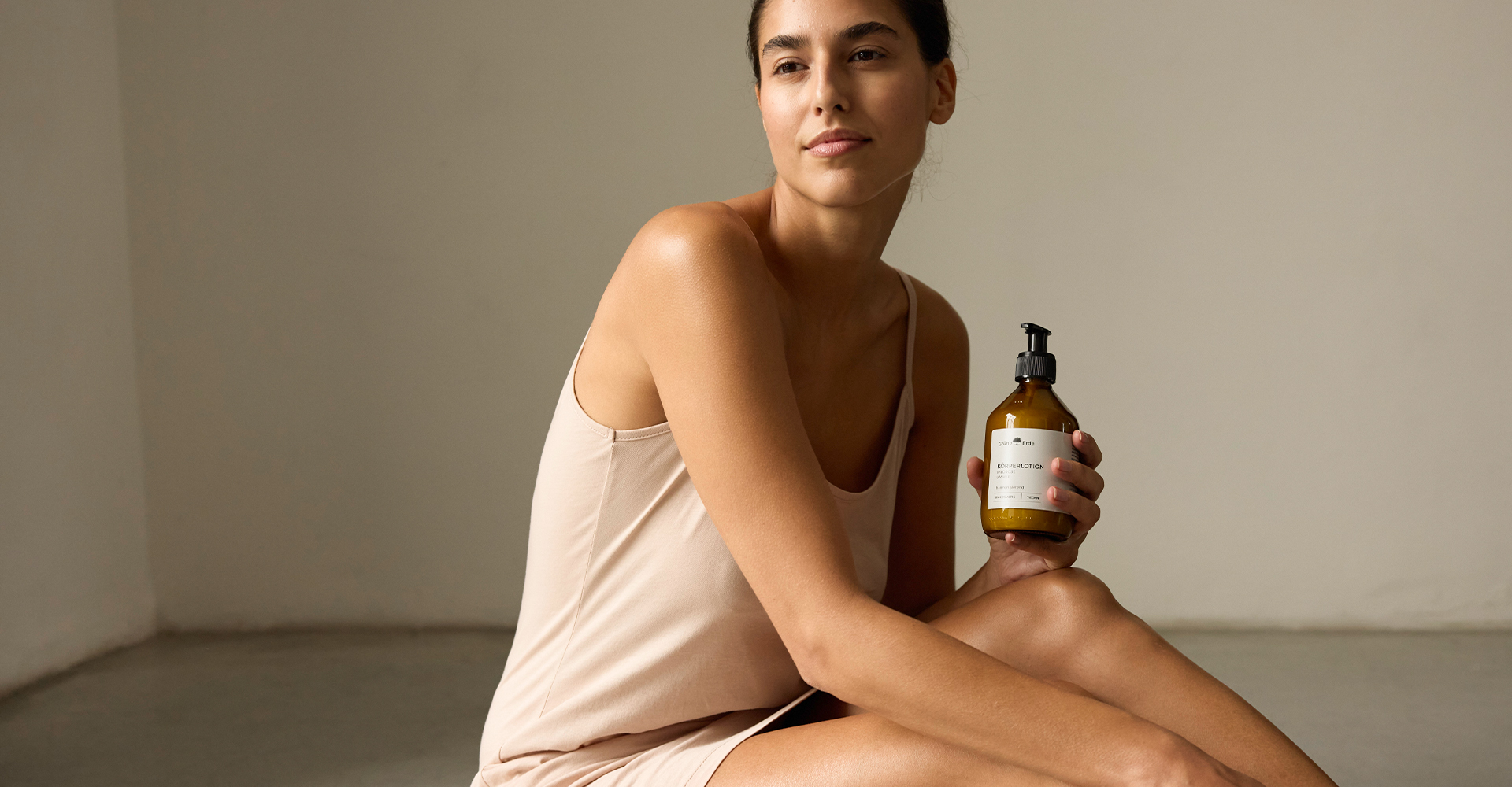Frau sitzt auf dem Boden und präsentiert eine Körperlotion in der Glasflasche mit Pumpspender