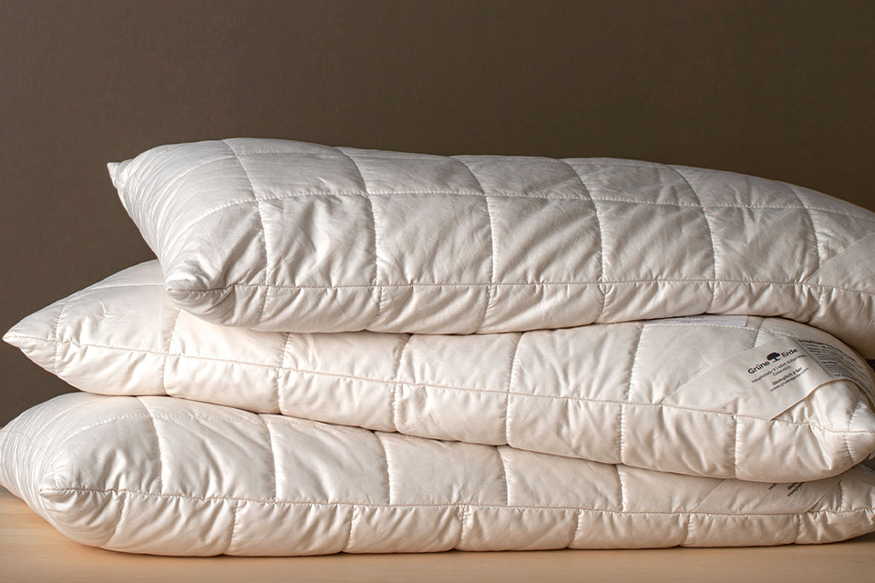 Drei hochwertige Komfortkissen liegen auf einem Stapel vor einer braunen Wand