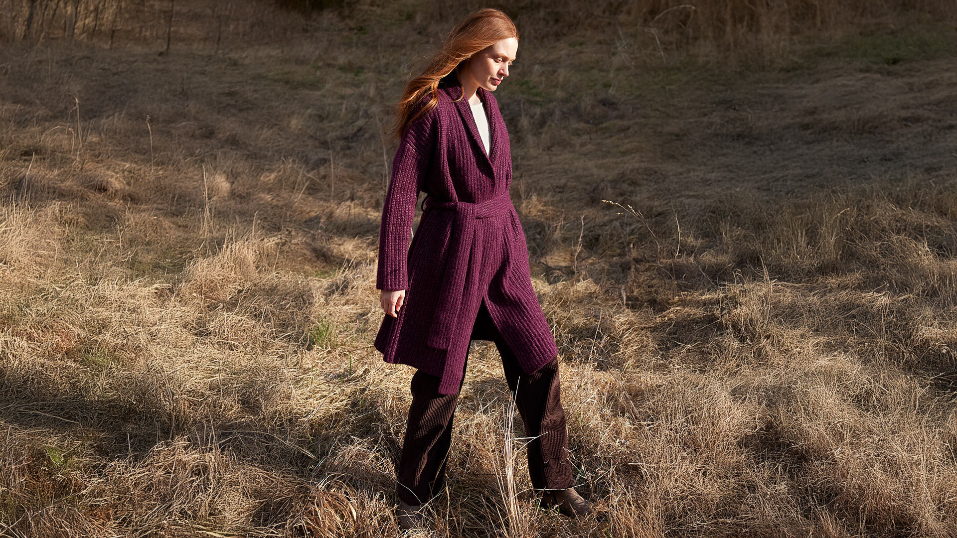 Frau in weiter Strickmode spaziert durch trockene Landschaft